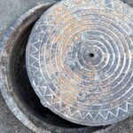 A close up of a manhole cover that's slightly open. The cover is hanging over the open hole just slightly to the right.