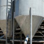 Two small industrial silos placed next to each other on a slab of concrete in front of a clear blue sky.