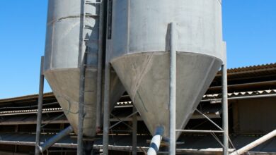 Two small industrial silos placed next to each other on a slab of concrete in front of a clear blue sky.