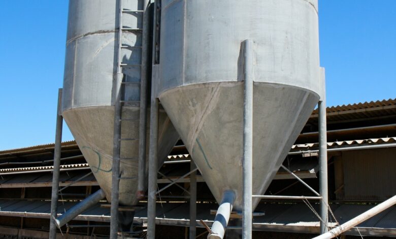 Two small industrial silos placed next to each other on a slab of concrete in front of a clear blue sky.