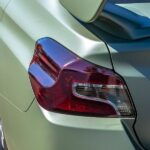 A close-up of the left taillight and spoiler of a vehicle. The car is matte green and parked on gravel.
