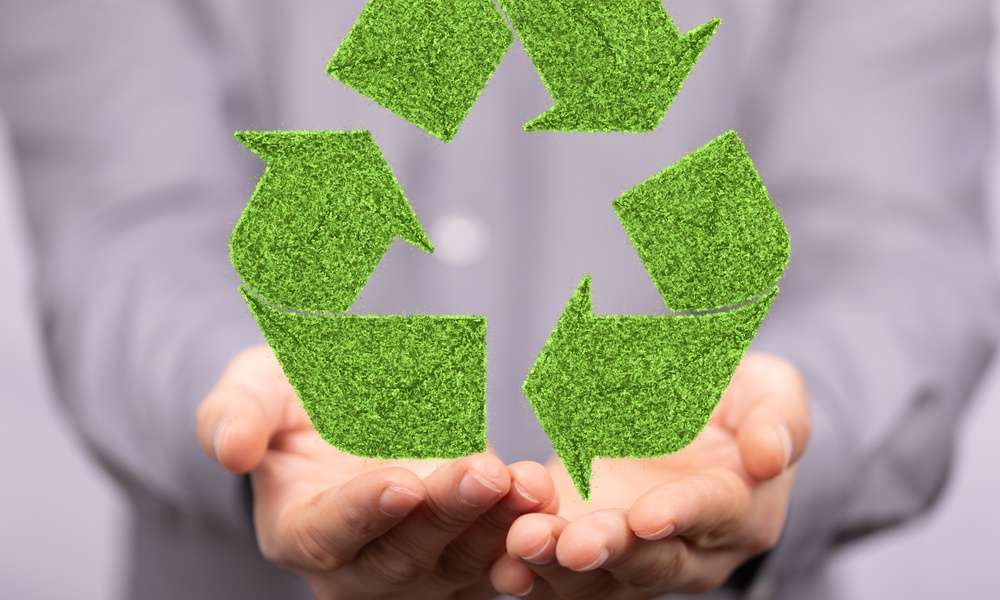 A person wearing a gray button down shirt holds out their hands to cradle a large green recycling symbol.