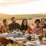 A person taking a photo of different people sitting at a large table outdoors. They are all smiling and laughing together.