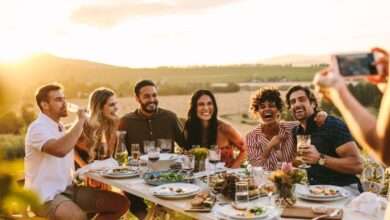 A person taking a photo of different people sitting at a large table outdoors. They are all smiling and laughing together.