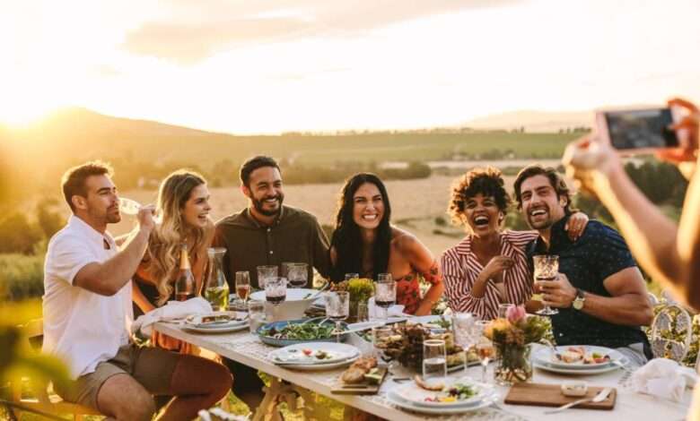 A person taking a photo of different people sitting at a large table outdoors. They are all smiling and laughing together.