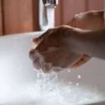 A close-up of someone washing their hands under running water. There's soapy water pooling in the sink.
