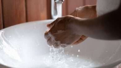 A close-up of someone washing their hands under running water. There's soapy water pooling in the sink.