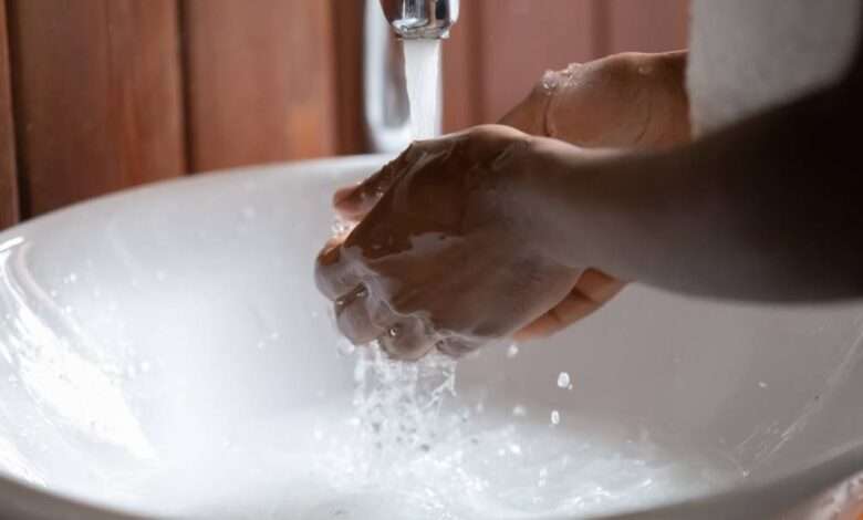 A close-up of someone washing their hands under running water. There's soapy water pooling in the sink.