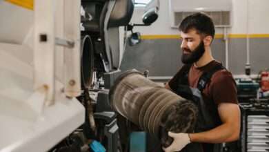 An auto mechanic wearing black overalls and white work gloves, taking out a dirty air filter from a fleet truck.