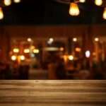 A close-up of a bar top with a blurred view of the bar's interior. There are Edison bulbs hanging from light fixtures.