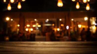 A close-up of a bar top with a blurred view of the bar's interior. There are Edison bulbs hanging from light fixtures.