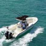 A single angler boat powered by motors moving across teal ocean waters. The passengers stand at the wheel.