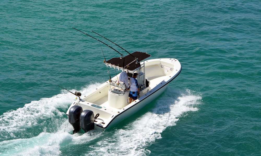 A single angler boat powered by motors moving across teal ocean waters. The passengers stand at the wheel.