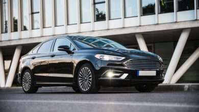A beautiful black sedan car is parked in front of a building. It is shiny, free of dings and dents, and looks like new.