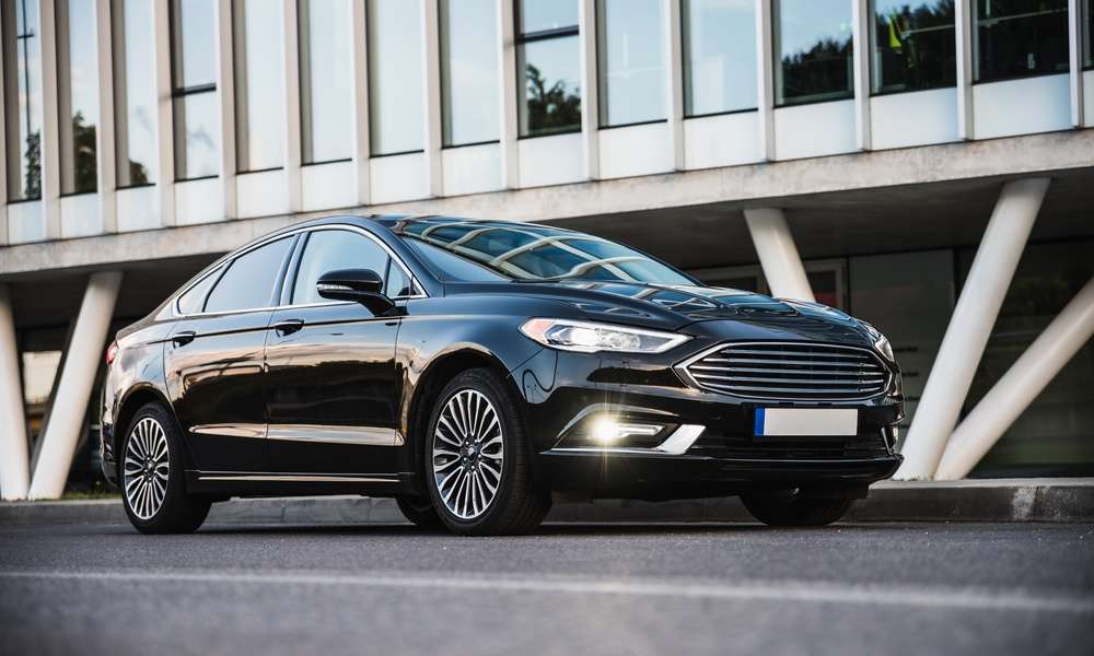 A beautiful black sedan car is parked in front of a building. It is shiny, free of dings and dents, and looks like new.