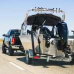 A black truck tows a large, silver boat behind it while driving along an uncrowded California interstate.