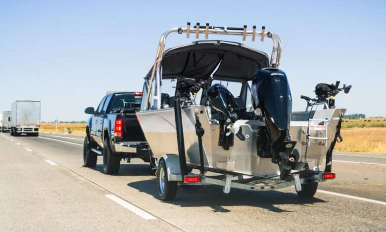 A black truck tows a large, silver boat behind it while driving along an uncrowded California interstate.
