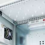 A metal enclosure houses a fan and an electric lamp mounted against smooth white interior surfaces.