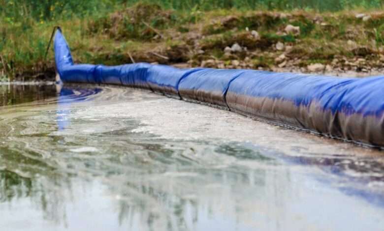 A close-up of a chemical spill on the ground near a grassy area. There is a long, inflated blue barrier stopping the spill.