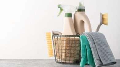 A close-up of brushes, sponges, rubber gloves, and natural cleaning products in a silver metal basket.