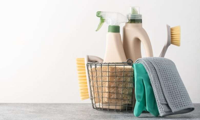 A close-up of brushes, sponges, rubber gloves, and natural cleaning products in a silver metal basket.
