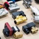 An assortment of eleven different solenoid valves that are all organized in a group by one another on a wooden surface.