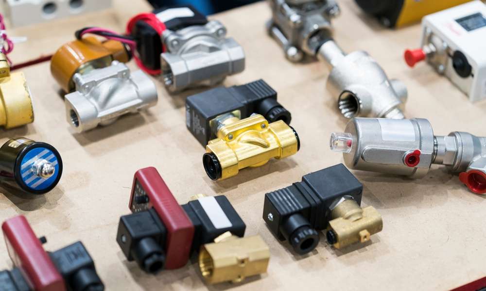 An assortment of eleven different solenoid valves that are all organized in a group by one another on a wooden surface.