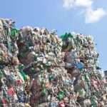 A close-up of a stack of plastic bottles for recycling in large, compact square piles against a blue sky.