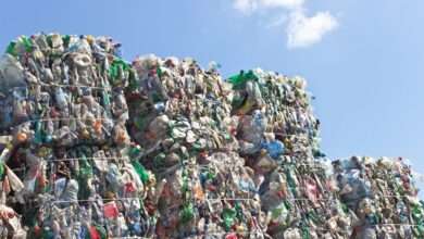 A close-up of a stack of plastic bottles for recycling in large, compact square piles against a blue sky.