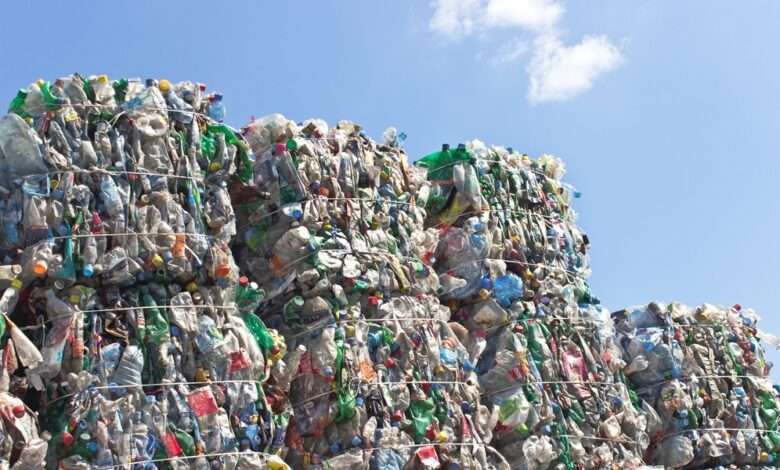 A close-up of a stack of plastic bottles for recycling in large, compact square piles against a blue sky.