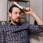 A close-up of a bearded man sits on the couch and hits his head with a dictionary, hoping that he will finally remember the definition.