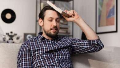 A close-up of a bearded man sits on the couch and hits his head with a dictionary, hoping that he will finally remember the definition.