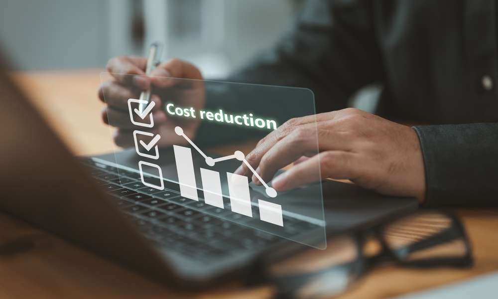 A digital illustration shows the words "Cost reduction" while a person's hands work on a laptop in the background.