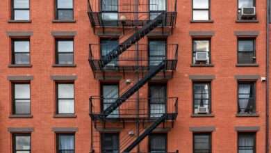 A close-up of an old red-brown brick apartment building in New York City. The fire escape staircase is black.