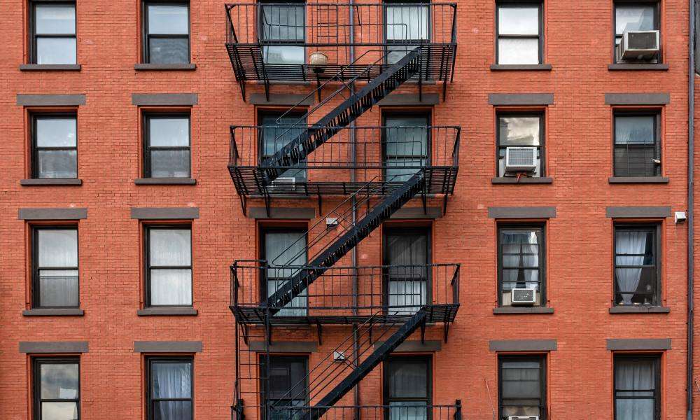 A close-up of an old red-brown brick apartment building in New York City. The fire escape staircase is black.