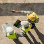 Above the heads of three engineers looking at a laptop on a construction site. They are all wearing hard hats.