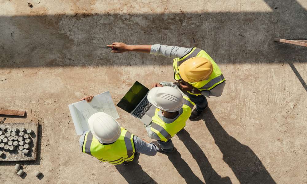 Above the heads of three engineers looking at a laptop on a construction site. They are all wearing hard hats.