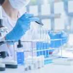 A close-up of a medical researcher in a white coat looking at a test tube of blue solution in a laboratory.