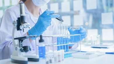 A close-up of a medical researcher in a white coat looking at a test tube of blue solution in a laboratory.