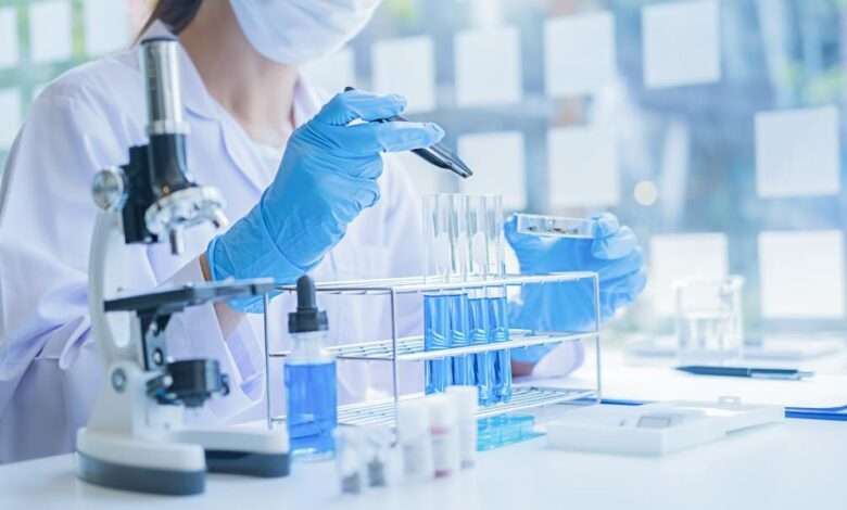 A close-up of a medical researcher in a white coat looking at a test tube of blue solution in a laboratory.