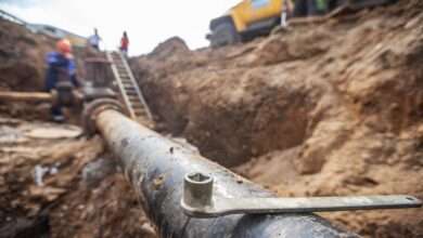 An underground pipeline that's been uncovered. There is a wrench balancing on top of it and some people in the background.
