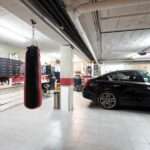 A black car is parked in a well-organized garage with a white tiled floor, exercise equipment, and storage solutions.