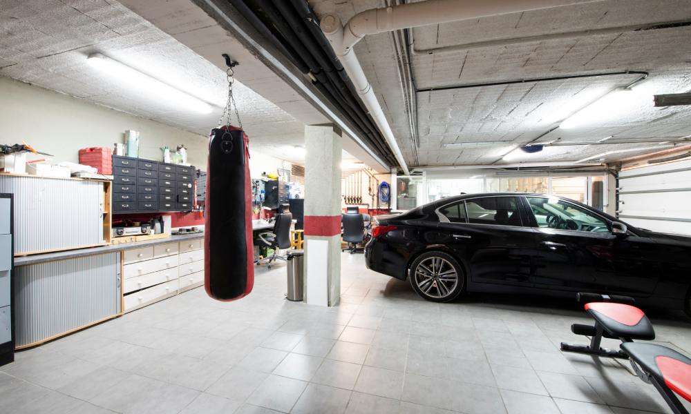 A black car is parked in a well-organized garage with a white tiled floor, exercise equipment, and storage solutions.