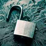 There is an unlocked padlock resting on top of a circuit board. The padlock has a rough finish.