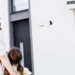 Three people, two adults and a child, stand in front of a home. There is a sale sign with a ‘sold’ sticker over it.