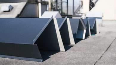 Several pieces of dark gray, angular metal flashing sit in a row on a textured roof awaiting installation.