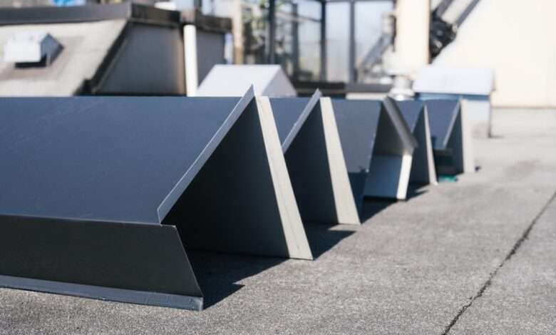 Several pieces of dark gray, angular metal flashing sit in a row on a textured roof awaiting installation.