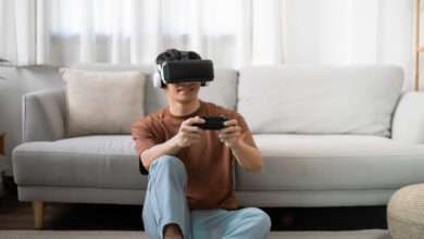 A teenage boy sitting on the floor in front of a couch, wearing a VR headset and holding a controller.