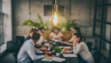 A close-up of a group of young creative business people meeting at the office with a bright yellow light bulb hanging above.