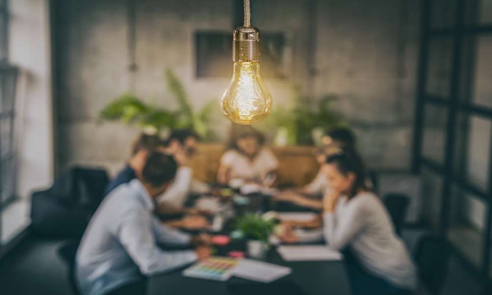 A close-up of a group of young creative business people meeting at the office with a bright yellow light bulb hanging above.